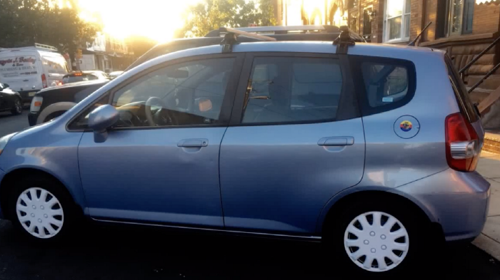 a new honda fit (compact car) that is light blue with white hubcaps.